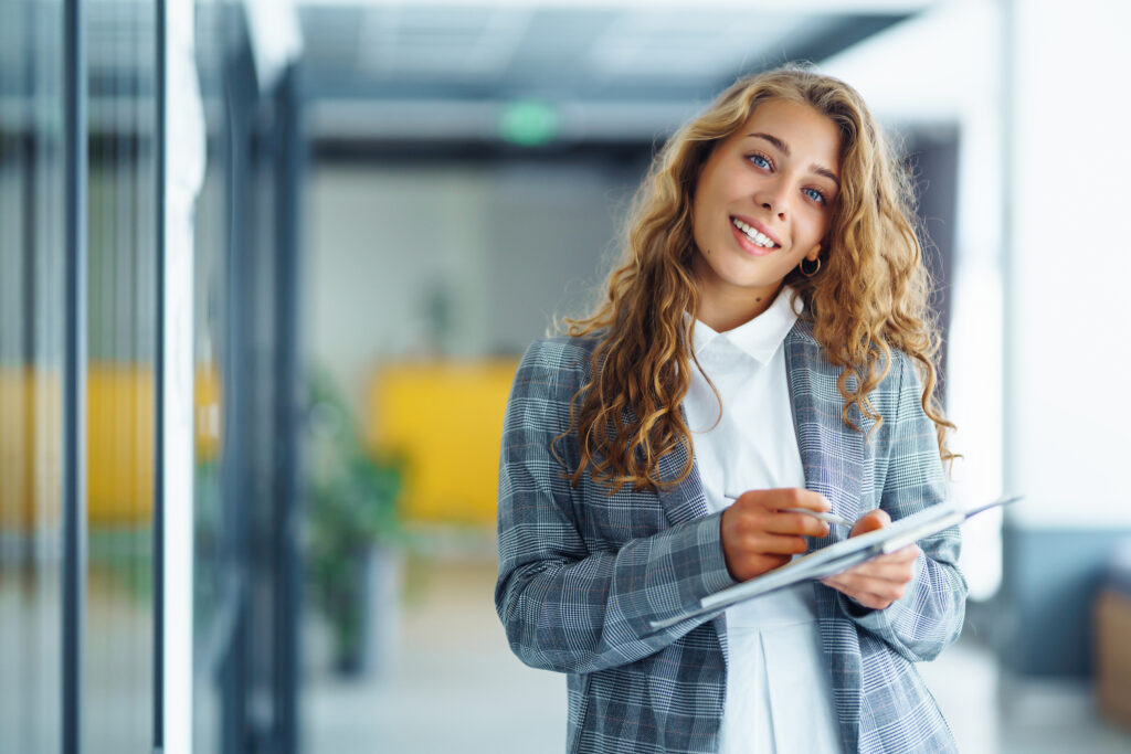 Portrait of business woman standing against office interior back
